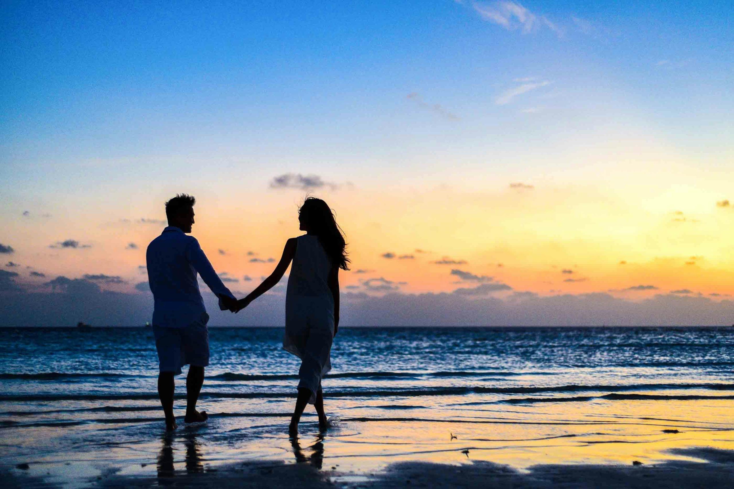Pareja caminando de la mano por la playa al atardecer, simbolizando la conexión y el amor consciente. Este escenario refleja la importancia de construir relaciones sanas y significativas. Al fondo, nuestra psiquiatra, psicoterapeuta y escritora María Fernanda, experta en salud emocional y desarrollo personal. Ella desarrolla contenido especializado para ayudar a las personas a atraer la pareja adecuada y fortalecer vínculos desde el amor propio y la autenticidad.