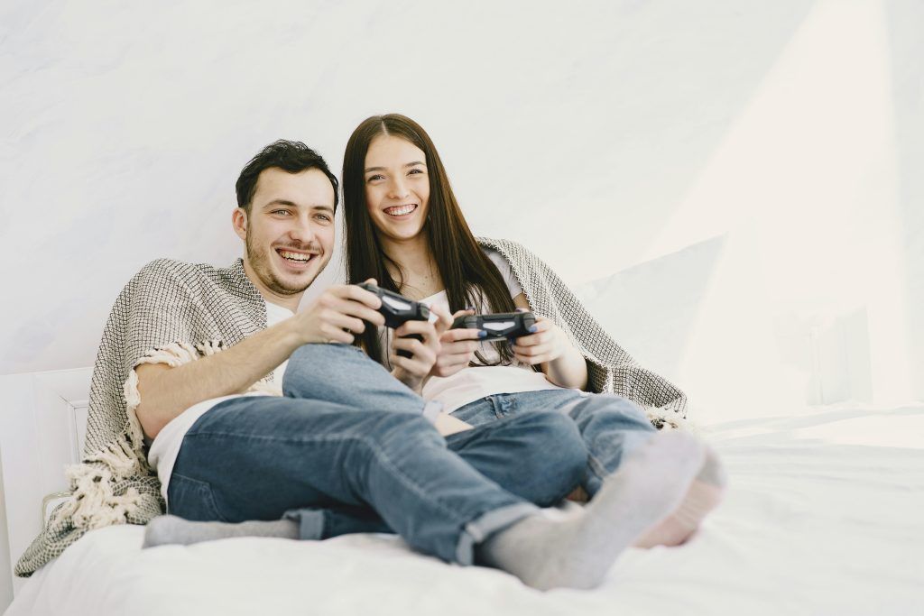 Pareja joven jugando videojuegos juntos en la cama, compartiendo momentos divertidos para romper la rutina y fortalecer su relación de forma lúdica.