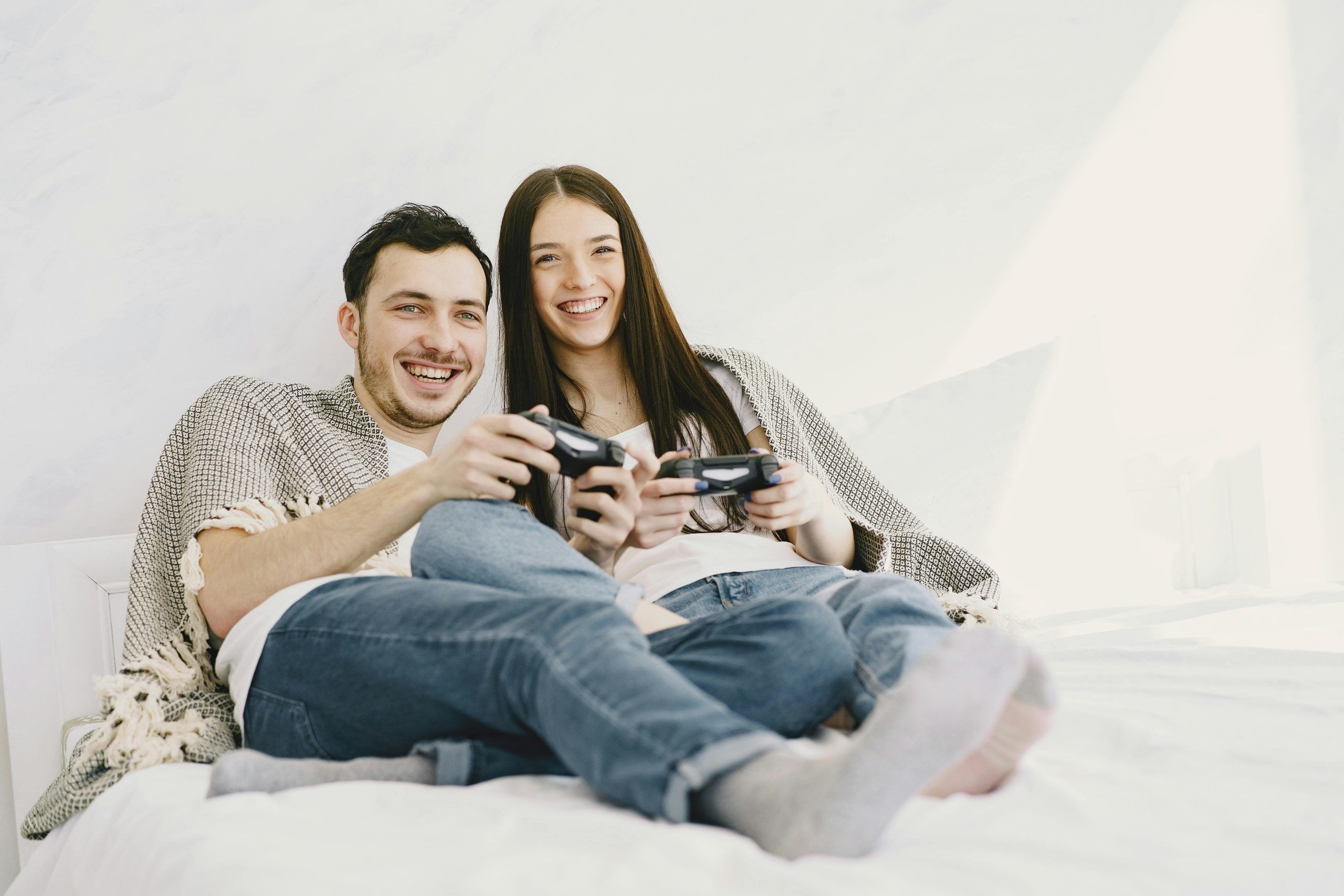 Pareja joven jugando videojuegos juntos en la cama, compartiendo momentos divertidos para romper la rutina y fortalecer su relación de forma lúdica.