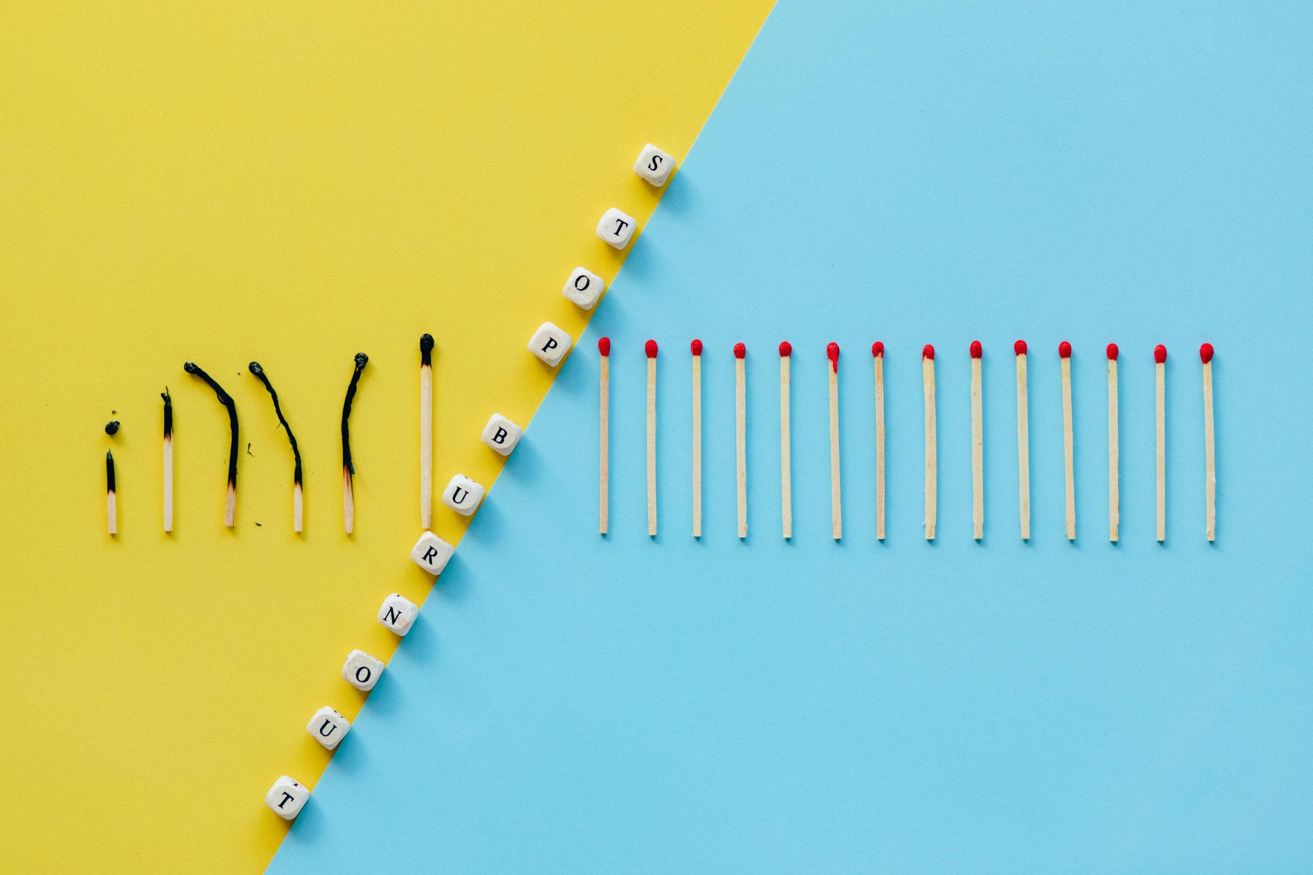 Imagen de dos colores divididos por dados que leen "Stop burnout". Un lado muestra un color amarillo con cerillos quemados, mientras que el otro lado es azul cielo con cerillos enteros. Los cerillos enteros son más numerosos, representando el síndrome de Procusto en el trabajo y su impacto en el bienestar laboral.