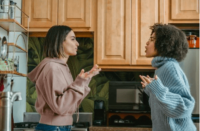Imagen de dos mujeres en conflicto en una habirtacion que parece una cocina, ninguna de las dos parece ceder ante una situacion que podria mejorar si conversan amablemente sobre el tema en cuestion.
